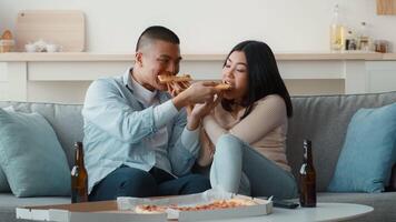 Two people sit on a comfortable sofa, playfully sharing slices of pizza. They relax together in a warm, inviting living room decorated with soft cushions and natural light. video