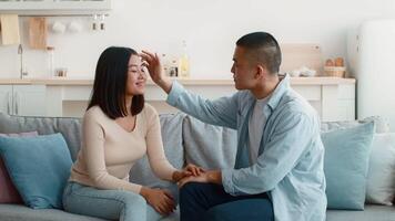 A young couple shares a sweet, intimate moment in a bright living room. They smile at each other while holding hands, enjoying each other's company in a casual, relaxed setting. video