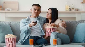 un Pareja disfruta un acogedor noche a hogar, sentado en un sofá con palomitas de maiz y bebidas ellos parecer comprometido en un película, compartiendo un relajado momento juntos. video