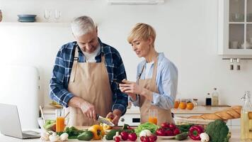 A couple collaborates in a stylish kitchen, chopping vegetables and discussing recipes while enjoying fresh produce and smoothies. The atmosphere is lively and creative. video