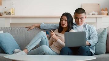 A couple sits comfortably on a couch, engaged with a laptop. She looks at him with a smile while he focuses on the screen. Cozy home setting creates a warm atmosphere. video