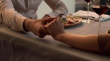 Two diners gently reach for a shared platter of food during a romantic evening meal, accompanied by glasses of wine on a stylish table with soft lighting. video
