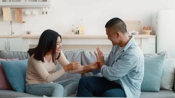 A young couple enjoys a lighthearted moment on a couch in their cozy living room. They are playfully teasing each other, laughing, and sharing a joyful atmosphere in the afternoon sun. video