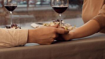 A couple sits at a cozy table, holding hands while sharing a plate of dessert and sipping red wine. The warm glow of sunset adds a romantic atmosphere to the evening. video