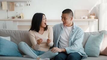 A couple sits on a couch in their cozy living room, sharing an excited moment as they look at a pregnancy test. Their facial expressions convey joy and anticipation about the future. video