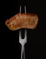 succulent slice of beef with tender texture and glossy caramelized glaze on a sleek two-prong fork highlighting rich flavor against a dark background photo