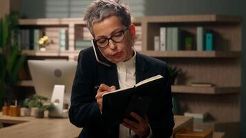 Stress busy multitasking business lady Caucasian senior woman middle-aged businesswoman mature female working in office talking phone writing notes answer call another smartphone talk with two phones video
