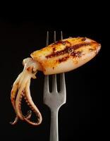 grilled squid on a sleek two-prong fork with charred grill marks and tender texture for seafood lovers on a dark background photo