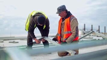 Construction of a new solar farm on a roof. Two engineers installing metal basis for future sunny batteries. Solar panels installation. video