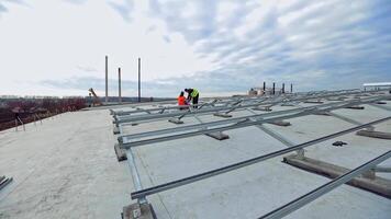 Future solar energy farm on a flat roof. Two workers in protective uniform installing metal basis for putting photovoltaic panels. video