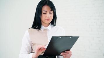 Portrait of a beautiful woman reading. Attractive brunette girl holding a folder and looking at the document on white studio background. video