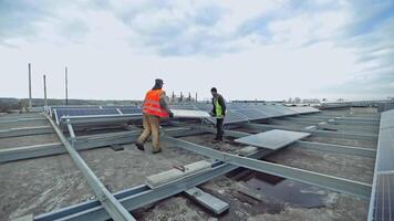 Technicians installing solar panel on metal base. Two workers laying down and installing solar panels on flat roof. PV panel converts solar energy into electric energy. video