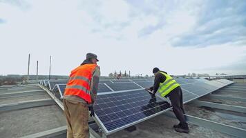 Installation of modernized solar farm. Two workers in a uniform installing photovoltaic panels on a metal basis. Renewable source of energy. video