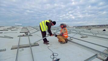 Workers building metal basis under blue cloudy sky. Two engineers in uniform constructing metal base for solar power plant on a roof. video