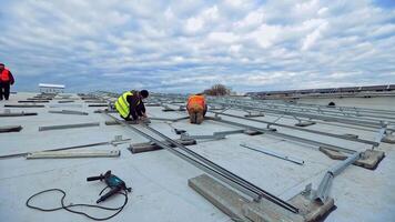 Workers on the roof of flat building. Engineers installing metal basis for future solar panels. Construction of solar farm for renewable energy. video