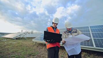 Technicians with plan and laptop on the solar farm. Workers in special uniform discussing the construction of solar panels to get clean energy. video
