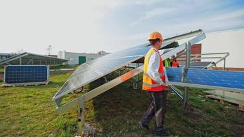 Workers install blue solar panel on the metal basis. Technicians in protective uniform and helmet attach sunny battery. Alternative source of energy. video