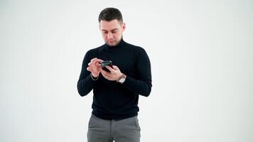 Creative businessman looking into the smartphone. Handsome man in black sweater using mobile phone isolated on white studio background. video