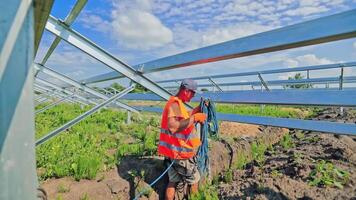 Building of an innovative solar power plant. Worker installing wires into the ground on the new solar farm in a bright summer day. video