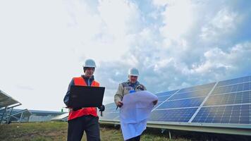 Workers in hard hat on the solar farm. Engineers talk about solar panels installation. Technicians with a laptop and project discuss the construction of new ecological station. video