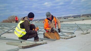 Works to construct solar panels. Two workers installing metal basis for sunny batteries on a flat roof of a huge building. Slow motion. video