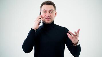 retrato do uma bonito homem falando a telefone. sério homem dentro Preto suéter fala em a Móvel telefone e dá alguns instruções dentro branco estúdio fundo. video