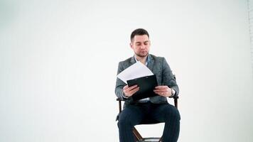 Serious businessman holding a folder and reading documents. Paper works flying over the handsome man in grey suit isolated on white studio background. video