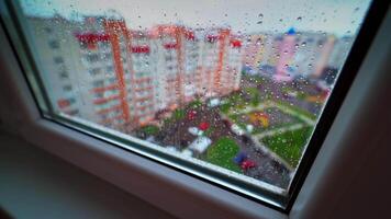 View through the window on raining weather. Drops of rain on a window pane on the city buildings background. Rain droplets flowing on a glass. video