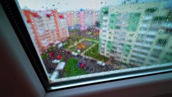 Rainy weather outside. View through the window with raindrops on glass on the background of colorful buildings in the city. video