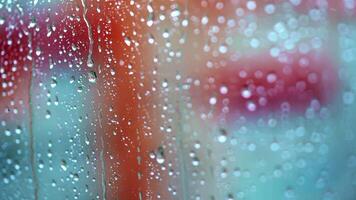 Glass window in a rainy day with drops. Transparent water of raindrops on a glass surface with red background. Close-up. video