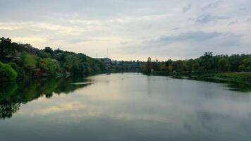 Calm water in the evening. River among green trees from both sides. Panoramic view of a river in the town. Motion camera back. Aerial view. video