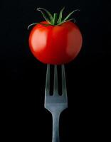 high-resolution photo of a vibrant fresh tomato on a sleek two-prong fork against a dark background for food photography and culinary designs