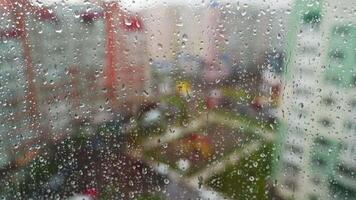 Wet window on blurred city background. Raindrops moving down on glass window at rainy weather. Water droplets on window pane. video