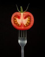 high-resolution photo of a fresh sliced tomato with vibrant seeds on a sleek two-prong fork against a dark background for food photography and culinary presentations