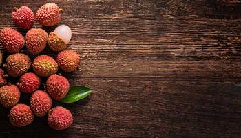 top-down view of fresh lychee fruits with pink-red textured skin and green leaves, arranged on a rustic wooden background, showcasing a peeled lychee revealing the white juicy flesh photo