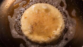 top view of pizza dough frying in bubbling hot oil creating crispy golden textures and detailed foamy surface photo