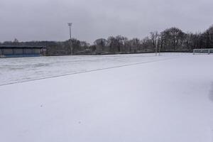 Snow covering soccer field during winter season with bleachers and cloudy sky photo