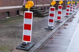 Red and white traffic barriers marking road construction zone on a rainy day photo
