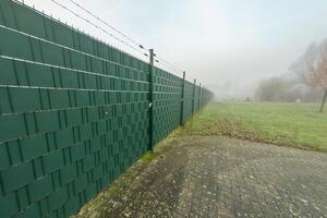 Green woven screen fence with barbed wire protecting property in foggy weather photo