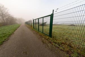 Barbed wire fence protecting solar panels along a misty brick path photo