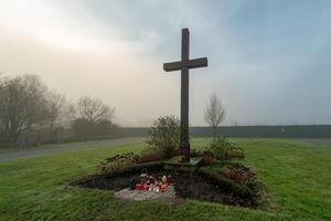 Large wooden cross standing in a foggy cemetery with candles photo