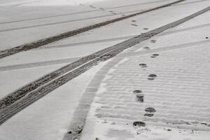 Footprints and tire tracks crossing on fresh snow surface photo