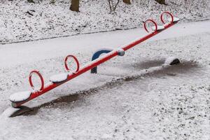 Red seesaw covered with snow in a playground during winter photo