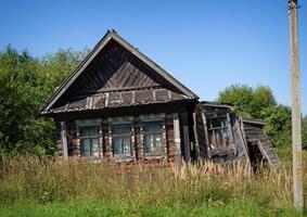 An old, abandoned log house. Deserted village in Russia. A lonely heart without people. Rotten wall construction. Hut against the background of the blue sky. photo