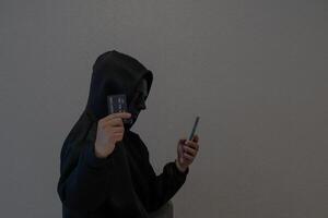 Side view Hacker, masked individuals holding phone and credit cards, cyber scams, criminal networks stealing information from call centers. photo