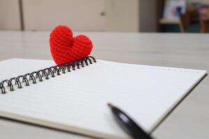 Side view. heart made of yarn on a notebook with pen and lines page for writing.Valentine Day Theme photo