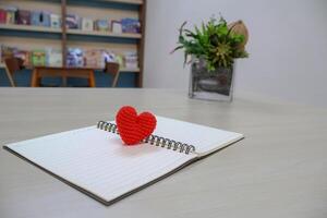 Side view. heart made of yarn on a notebook with lines page for writing with artificial flowers as decoration. Valentine Day Theme photo