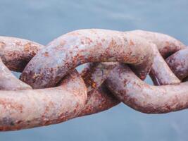 A close-up photo of a large iron chain from a cargo ship shows signs of rust due to the oxidation process from seawater