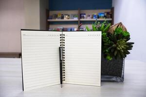 Notebook with lines page and black pen on wooden table background with artificial flowers as decoration. photo