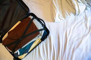 Open black suitcase with clothes packed for travelling on the bed photo